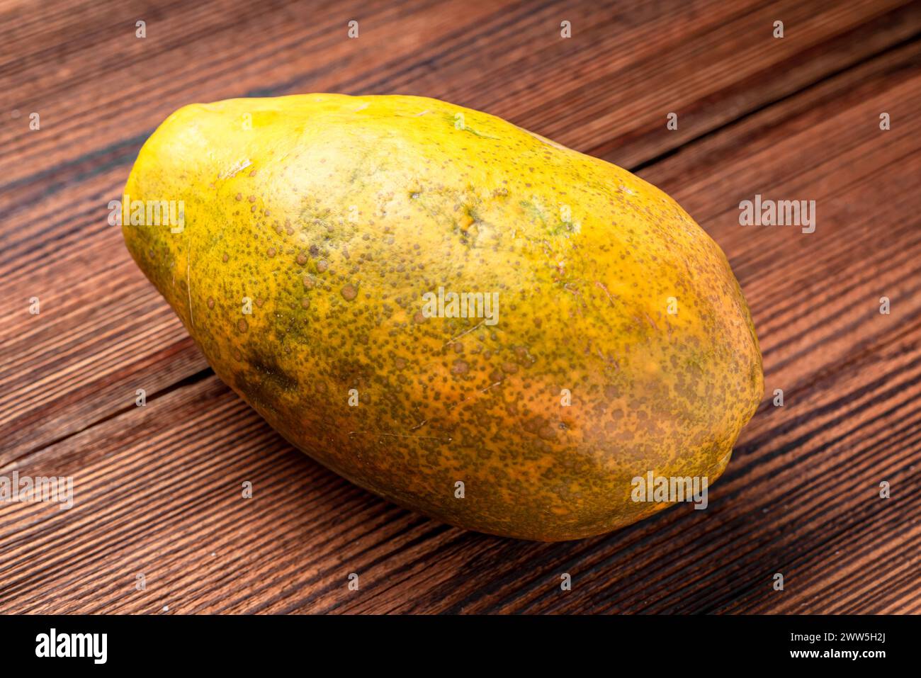 A large, yellow, and slightly wrinkled fruit sits on a wooden table ...