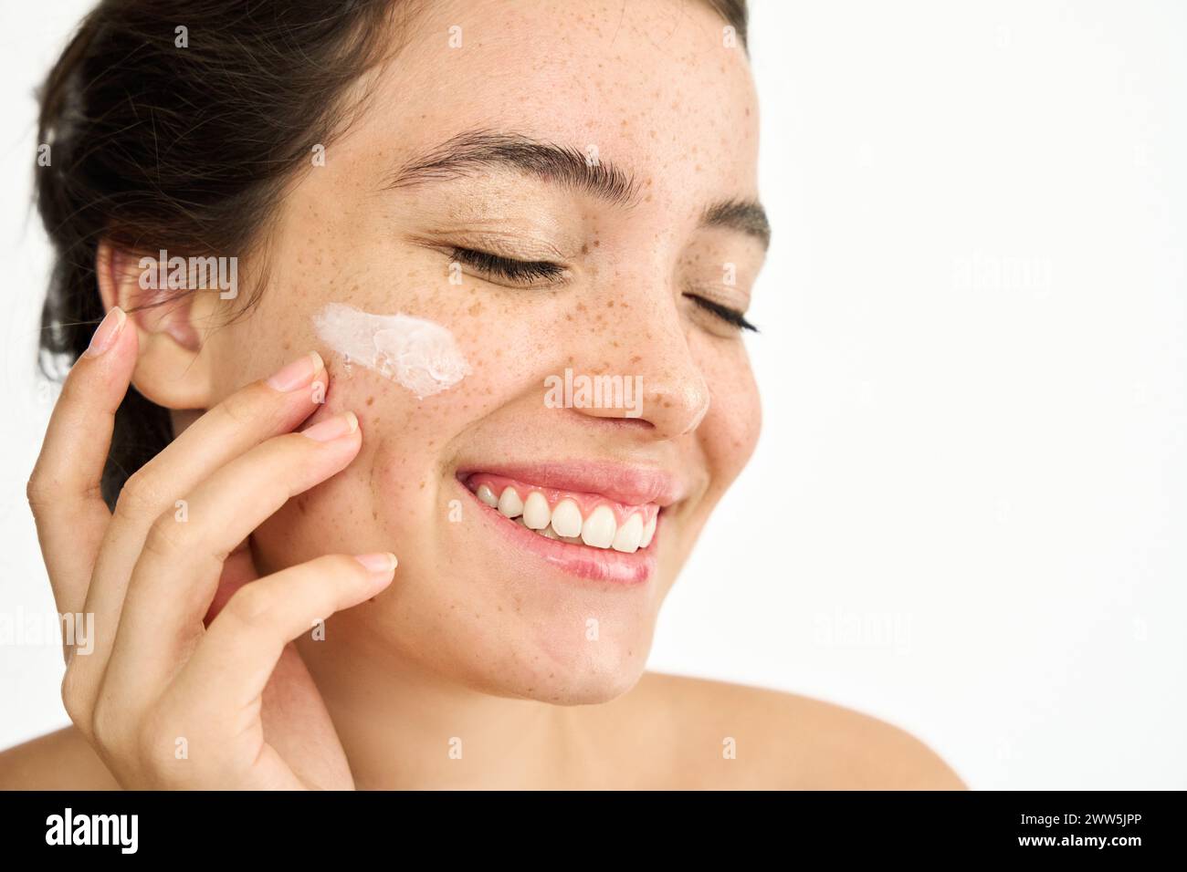 Happy Latin girl applying face cream isolated on white background, close up. Stock Photo