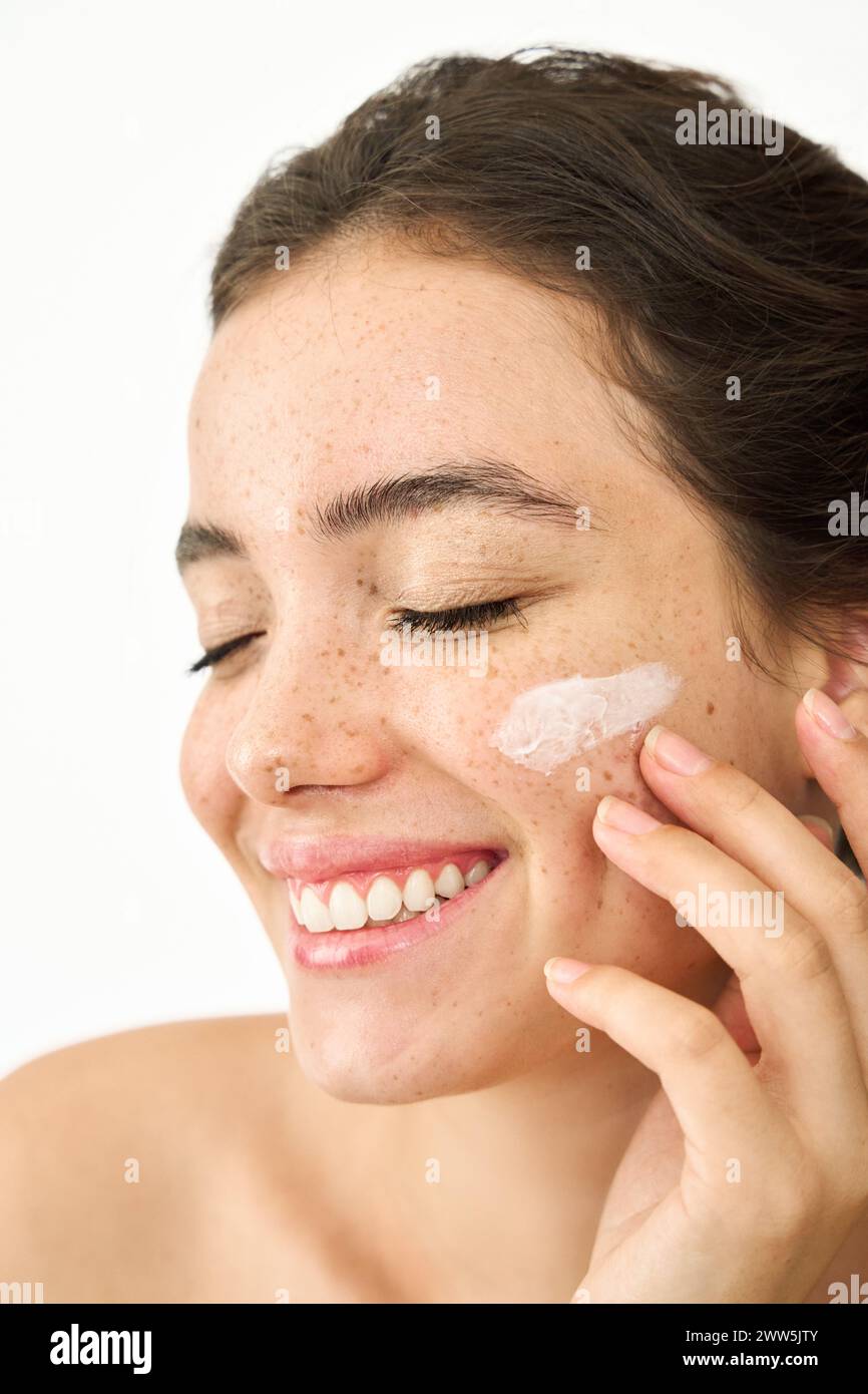 Happy Latin girl applying face cream isolated on white background, vertical. Stock Photo