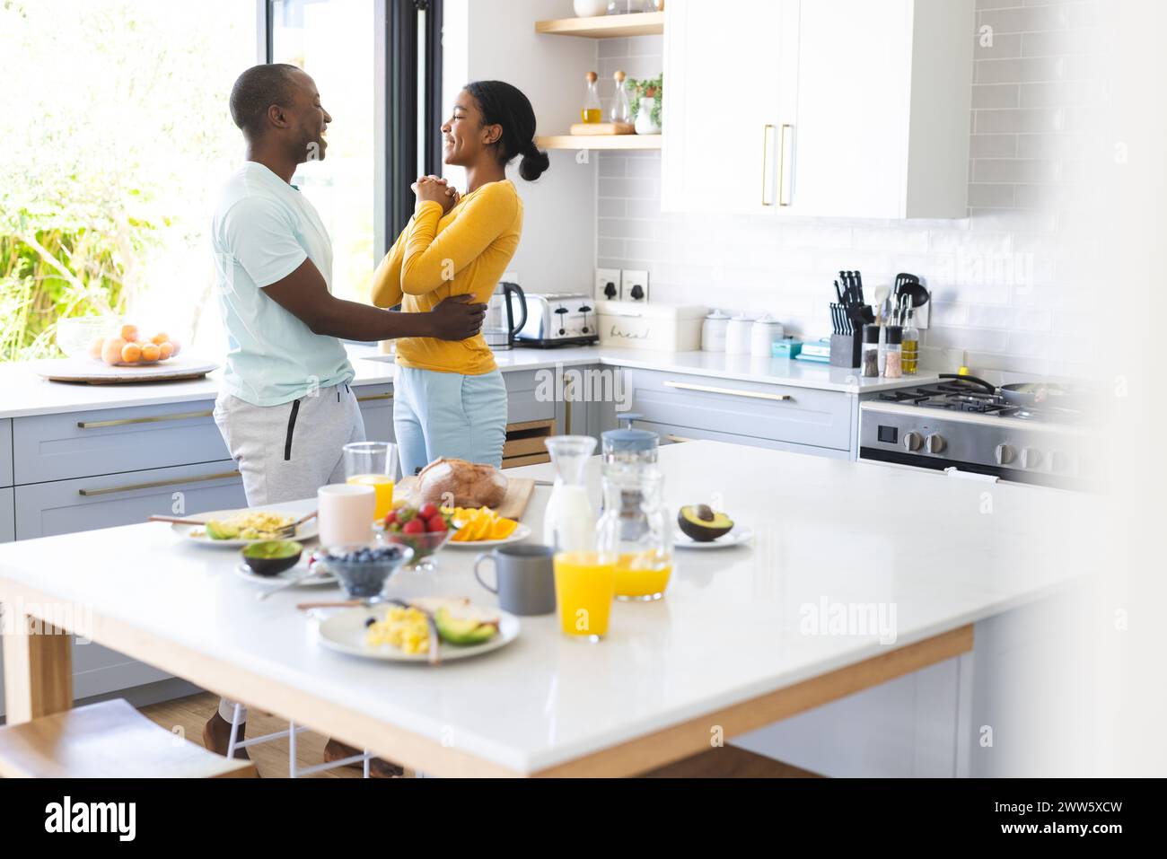 A diverse couple shares a moment in a sunlit kitchen at home at breakfast Stock Photo