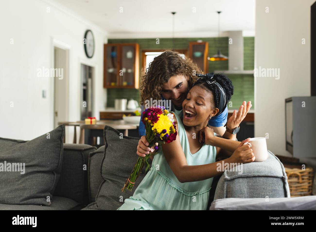 Caucasian man surprising African American woman with flowers at home on couch Stock Photo