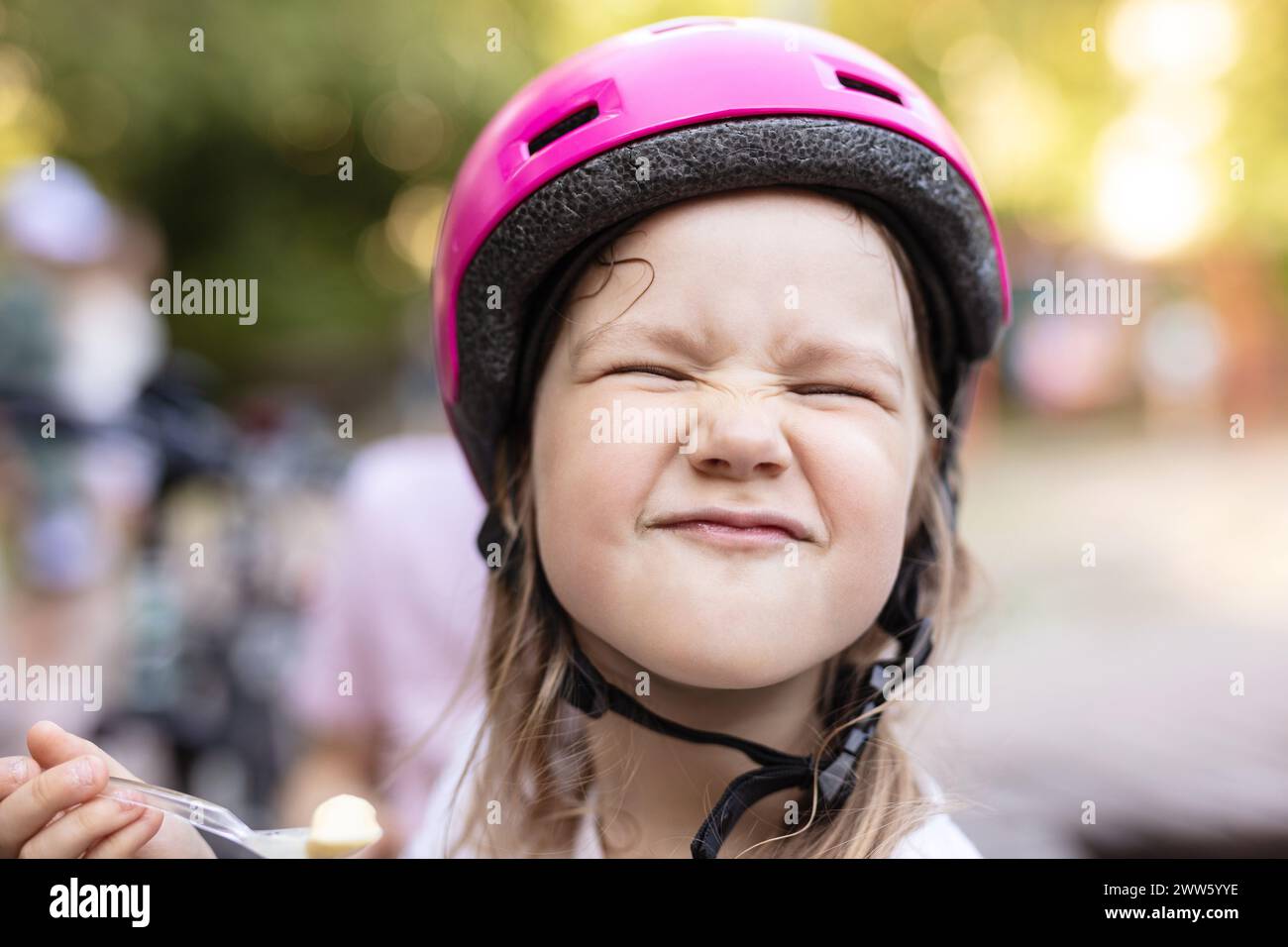 Cute young girl in helmet eating ice cream and making funny face Stock Photo