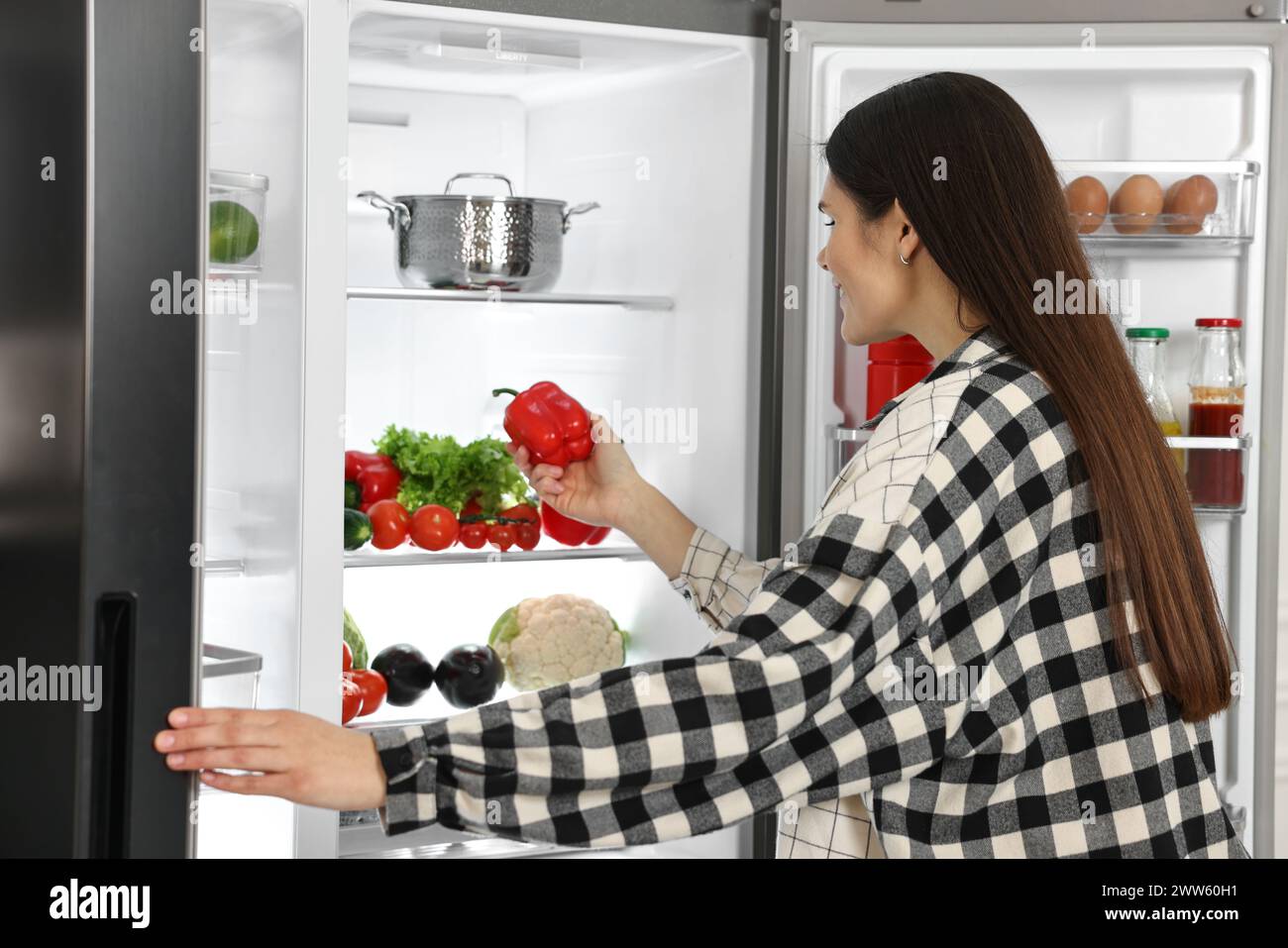 Young woman taking red bell pepper out of refrigerator Stock Photo Alamy