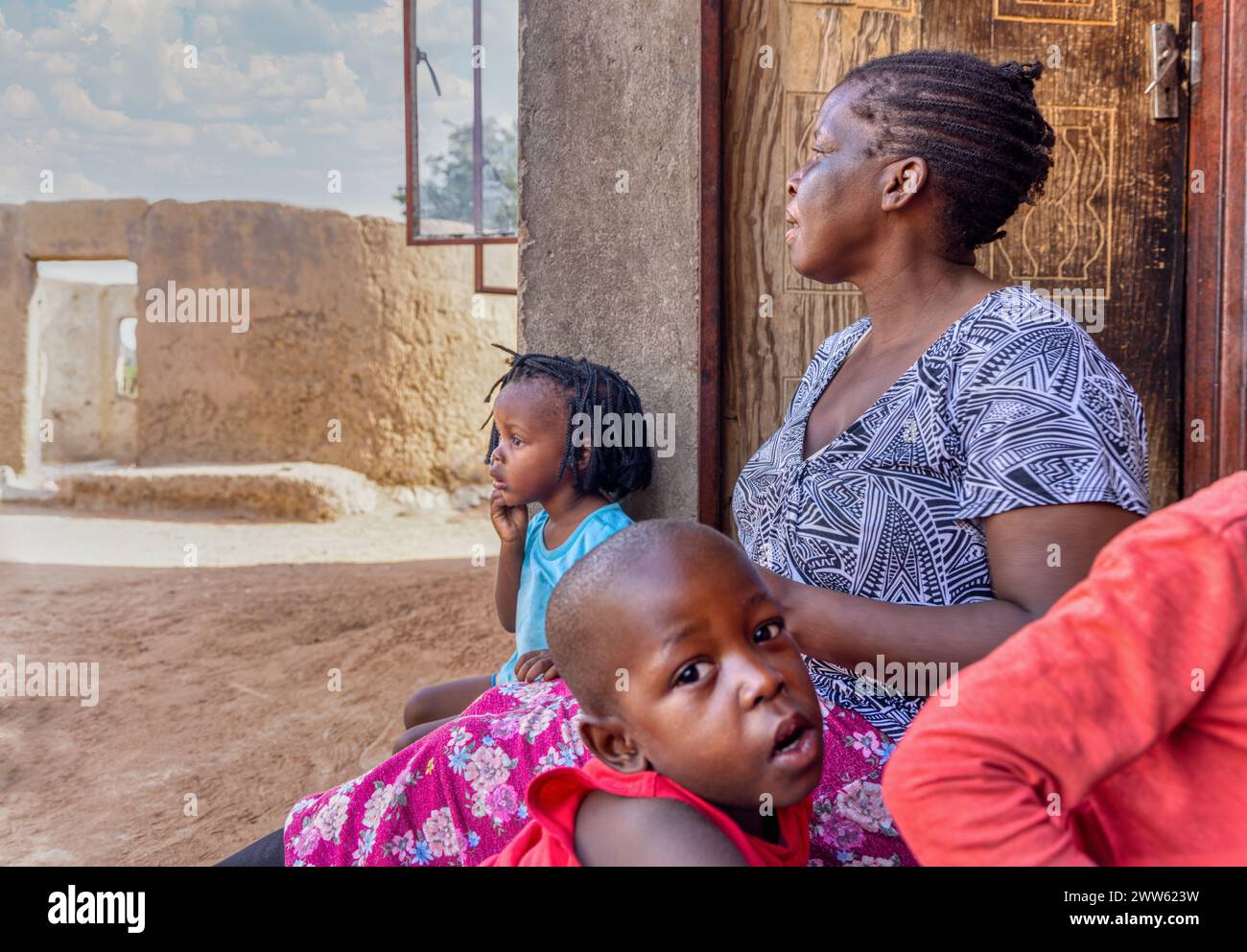 village african kids and mother sitting in front of the shack mud house Stock Photo