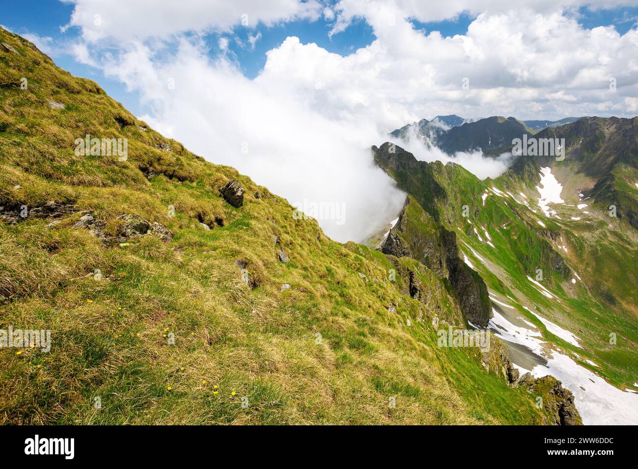 landscape of transylvania alps in summer. spots of snow among grass on the rocky slopes of fagaras range beneath a sky with clouds. popular travel des Stock Photo