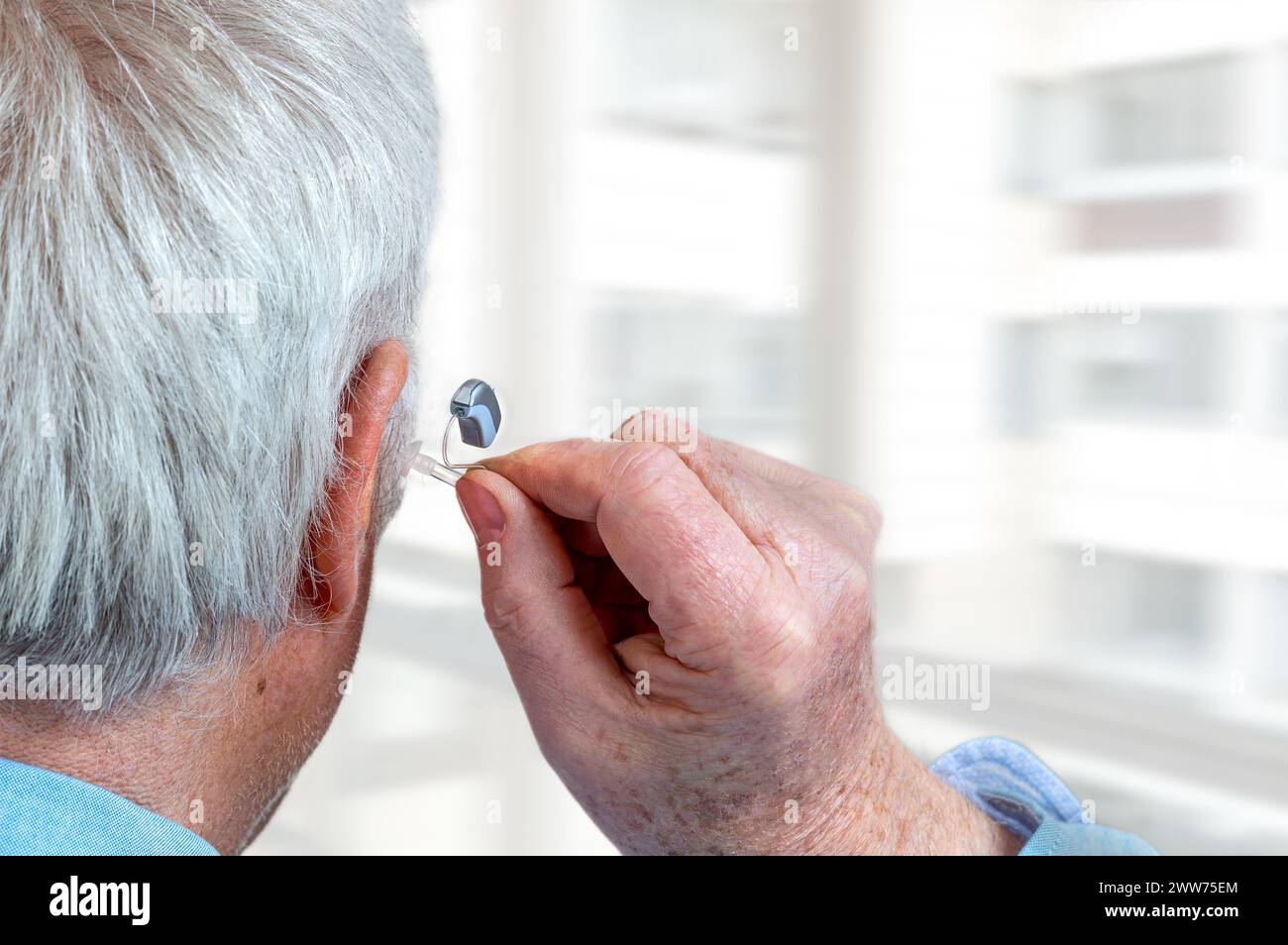 American shot of fitting a hearing aid to a white-haired senior citizen, rear view. Stock Photo