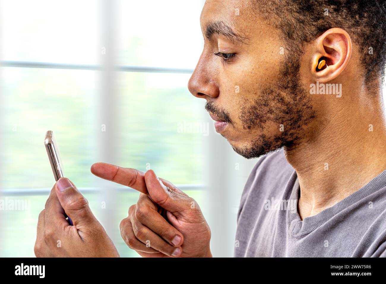 Young man adjusting the volume intensity of the hearing aid with the smartphone. Stock Photo