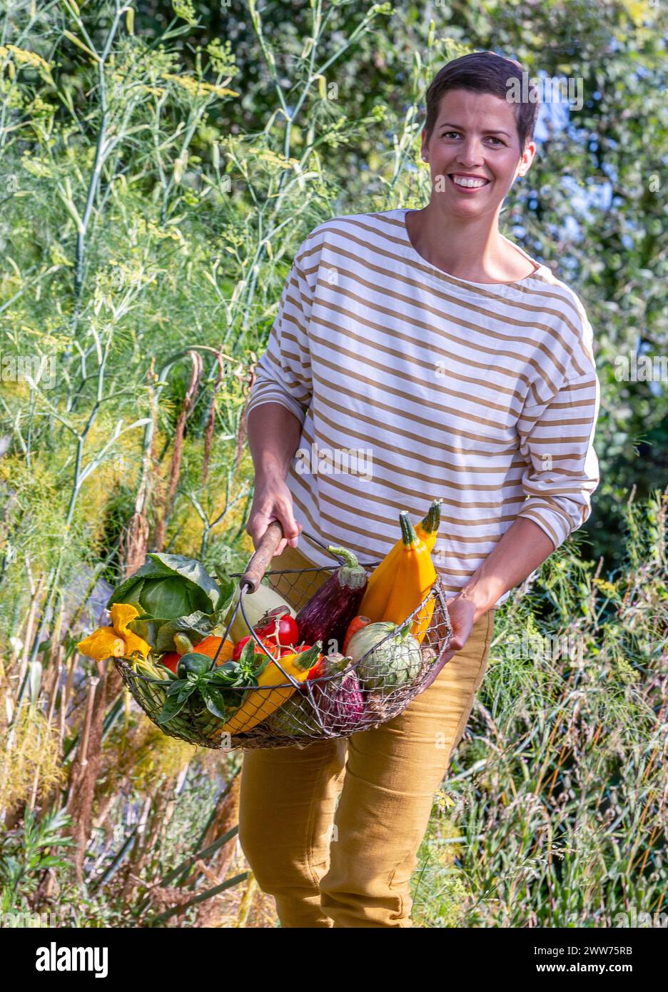 Woman in motion taking out the basket full of vegetables from the vegetable garden. Stock Photo