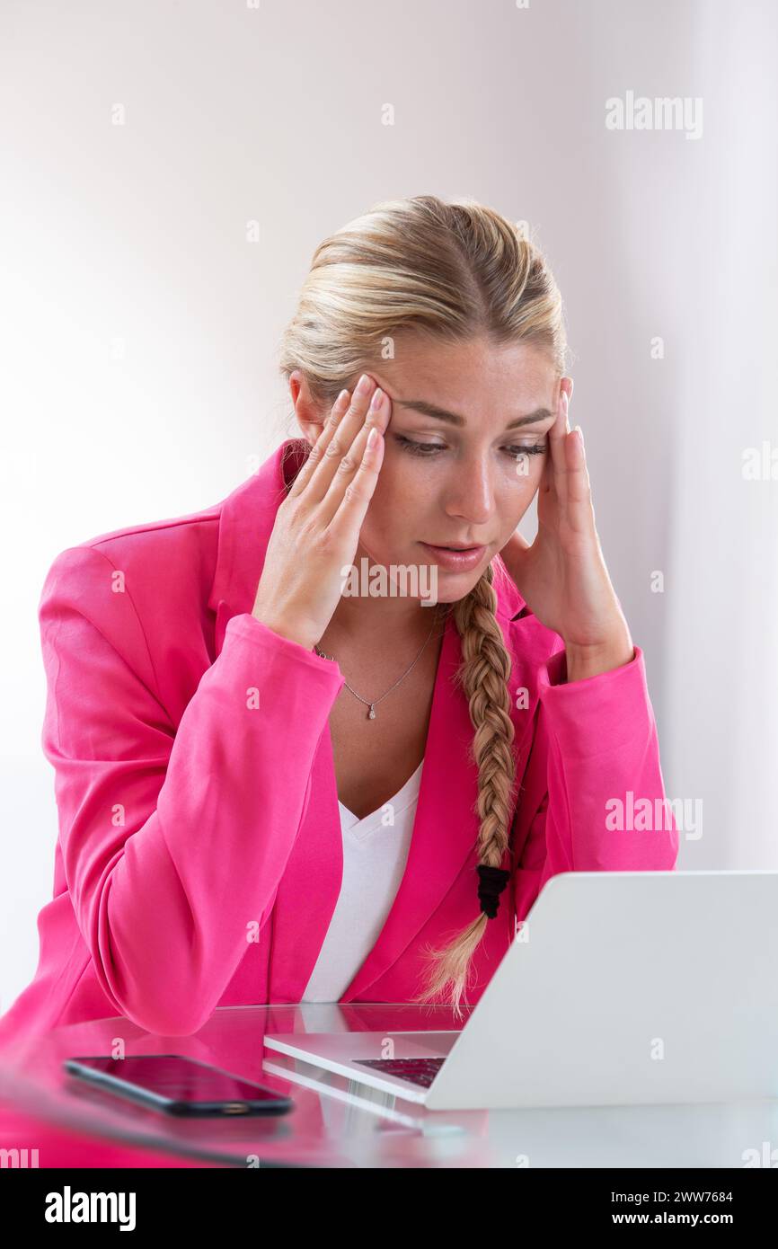 Woman facing her computer clutching her head with her fingers. their fingers. Stock Photo