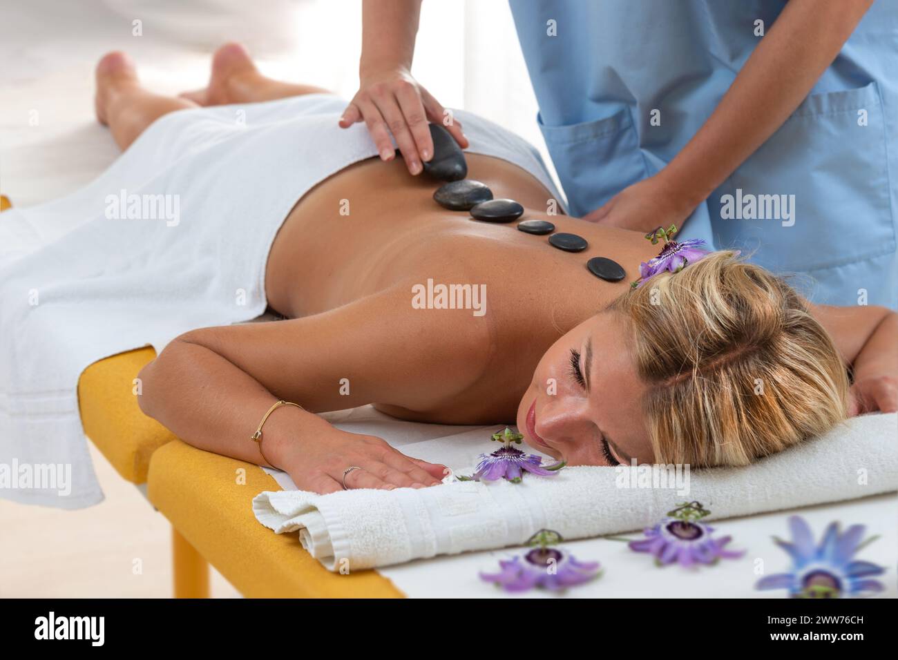 View from above - The masseur positions the basalt pebbles in the center of the young woman's back. Stock Photo