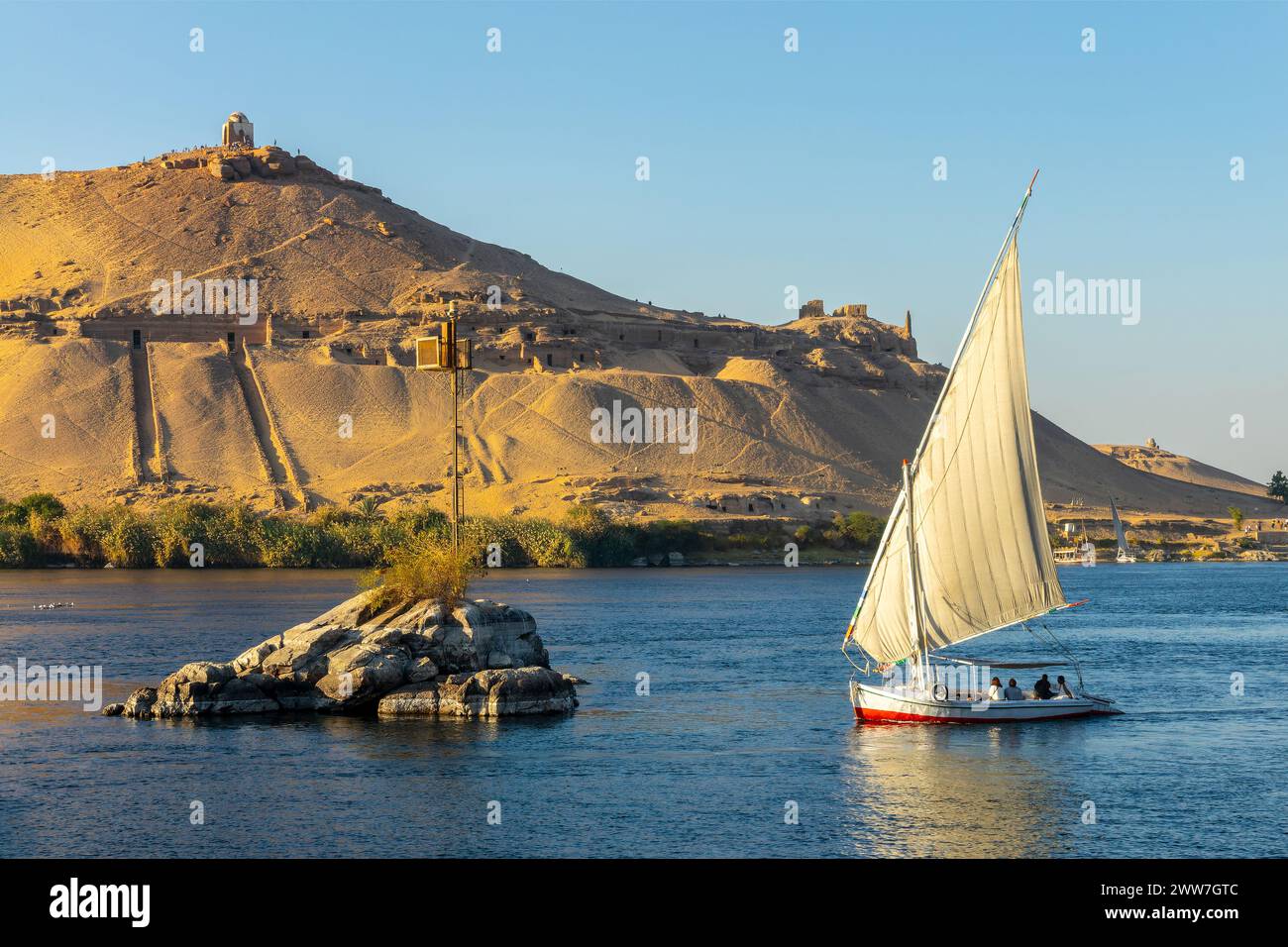 Felucca (traditinal egyptian sailing boat) on the Nile river and the Dome of Abu Al-Hawa (Qubbet el-Hawa) or Dome of the Wind in Aswan, Egypt Stock Photo
