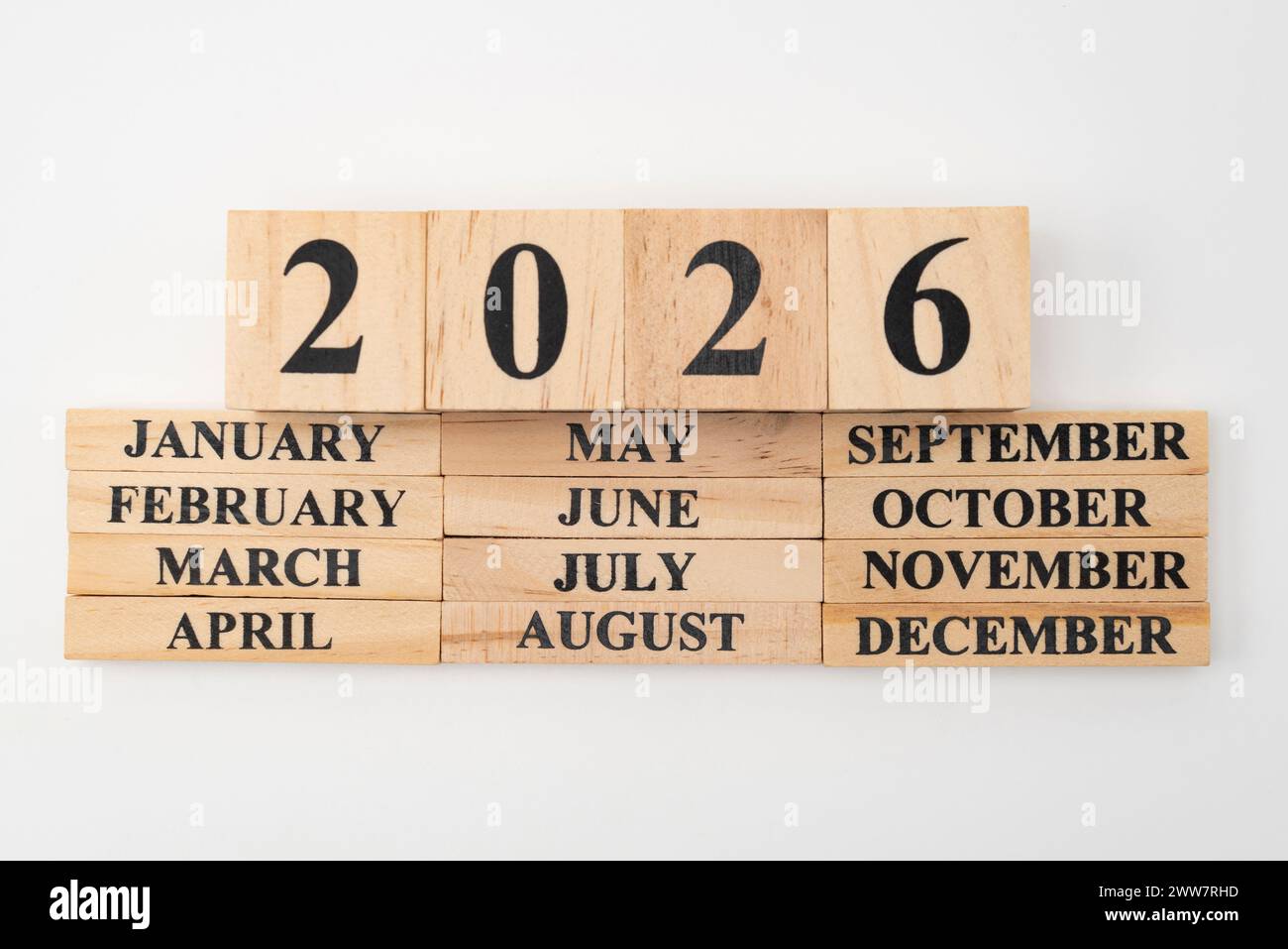 Year 2026 written on wooden cubes on top of the months of the year written on twelve rectangular pieces of wood. Isolated on white background. Stock Photo