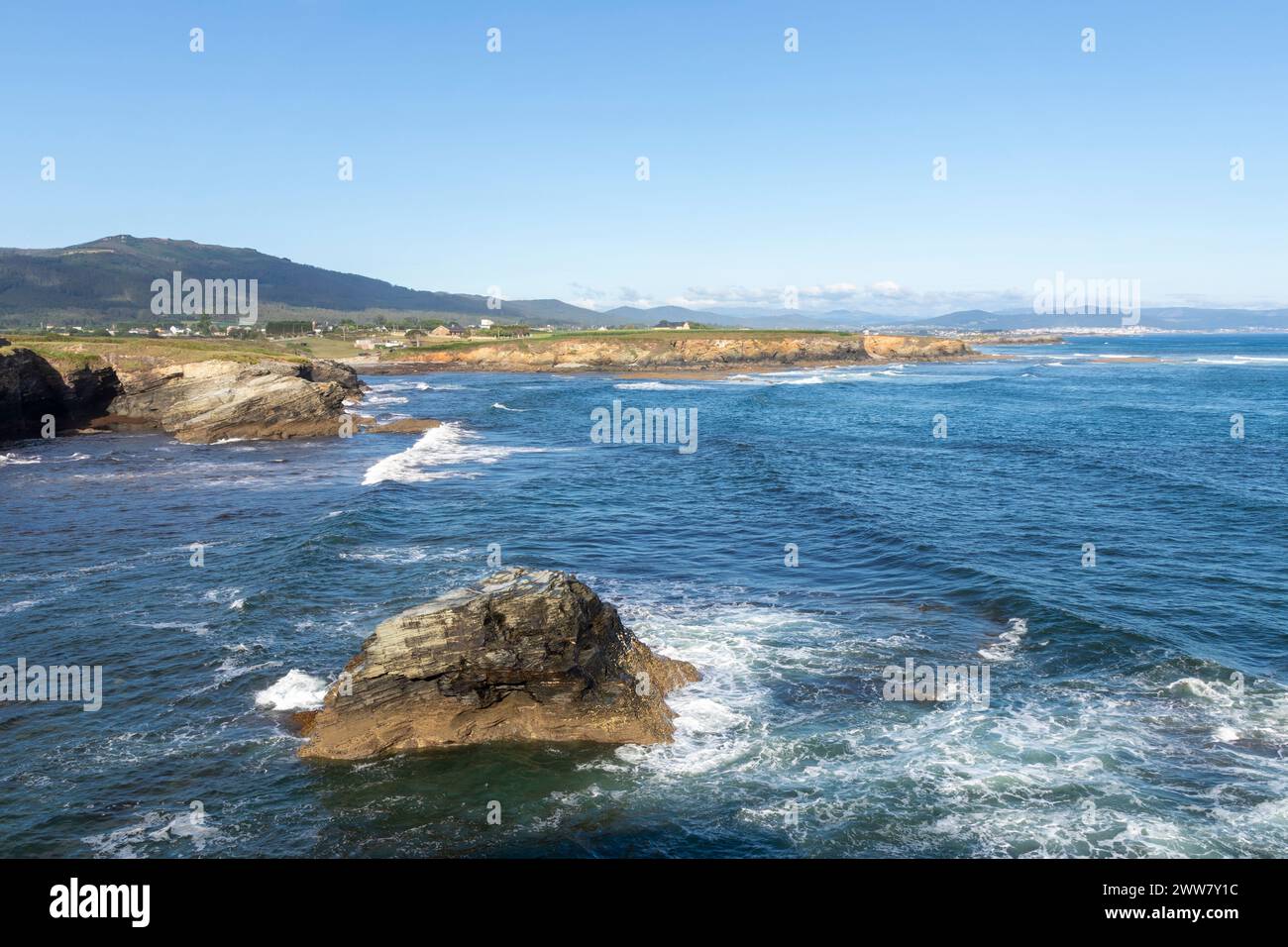 scenic coastline with rocky formations, blue waters, and distant mountains under a clear sky, exhibiting natural beauty Stock Photo
