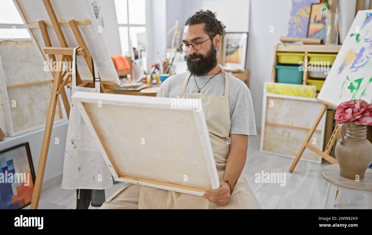 A young bearded man examines an empty canvas in a bright art studio ...