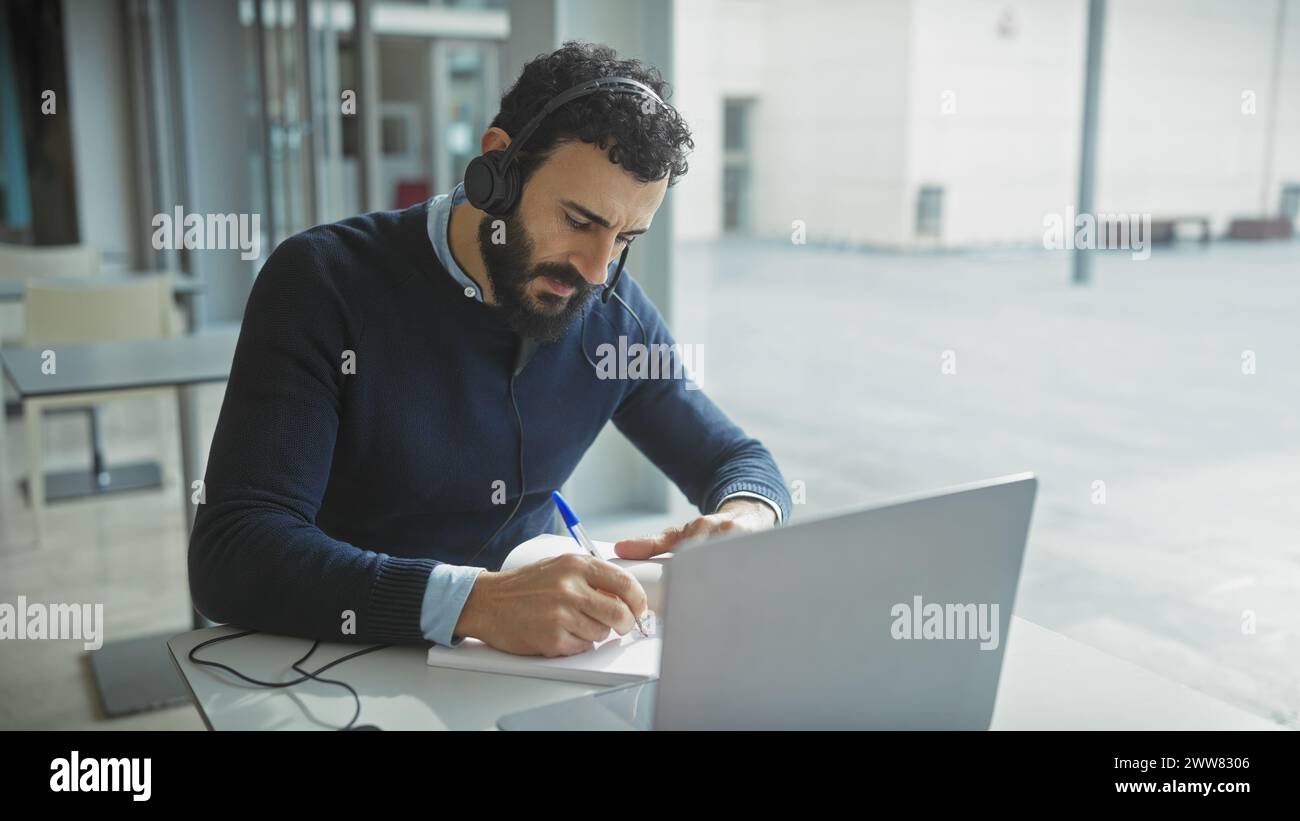 Bearded man telecommuting in a modern office, using headphones and ...