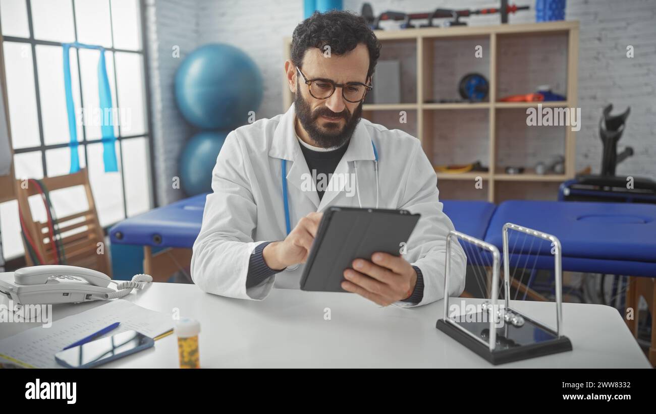 Middle-aged bearded man in lab coat using tablet at rehabilitation center clinic. Stock Photo