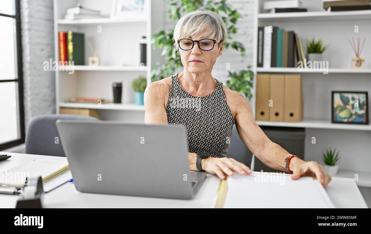 A mature woman with short grey hair works attentively at her laptop in ...