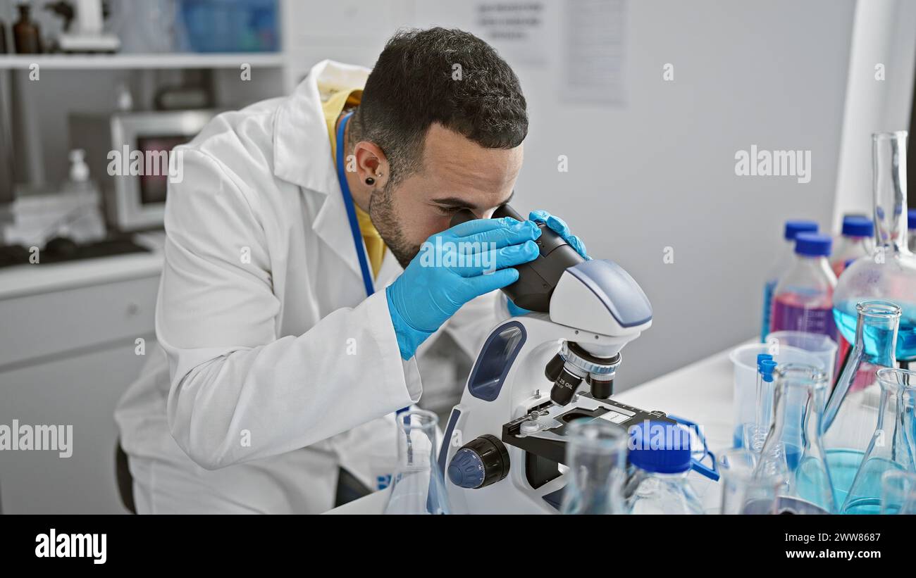 Hispanic scientist man analyzing samples using microscope in a laboratory setting Stock Photo