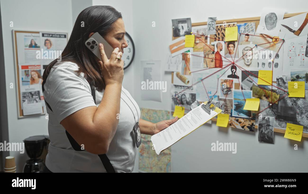 Hispanic woman detective analyzes evidence in an office with a crime investigation board while talking on the phone. Stock Photo