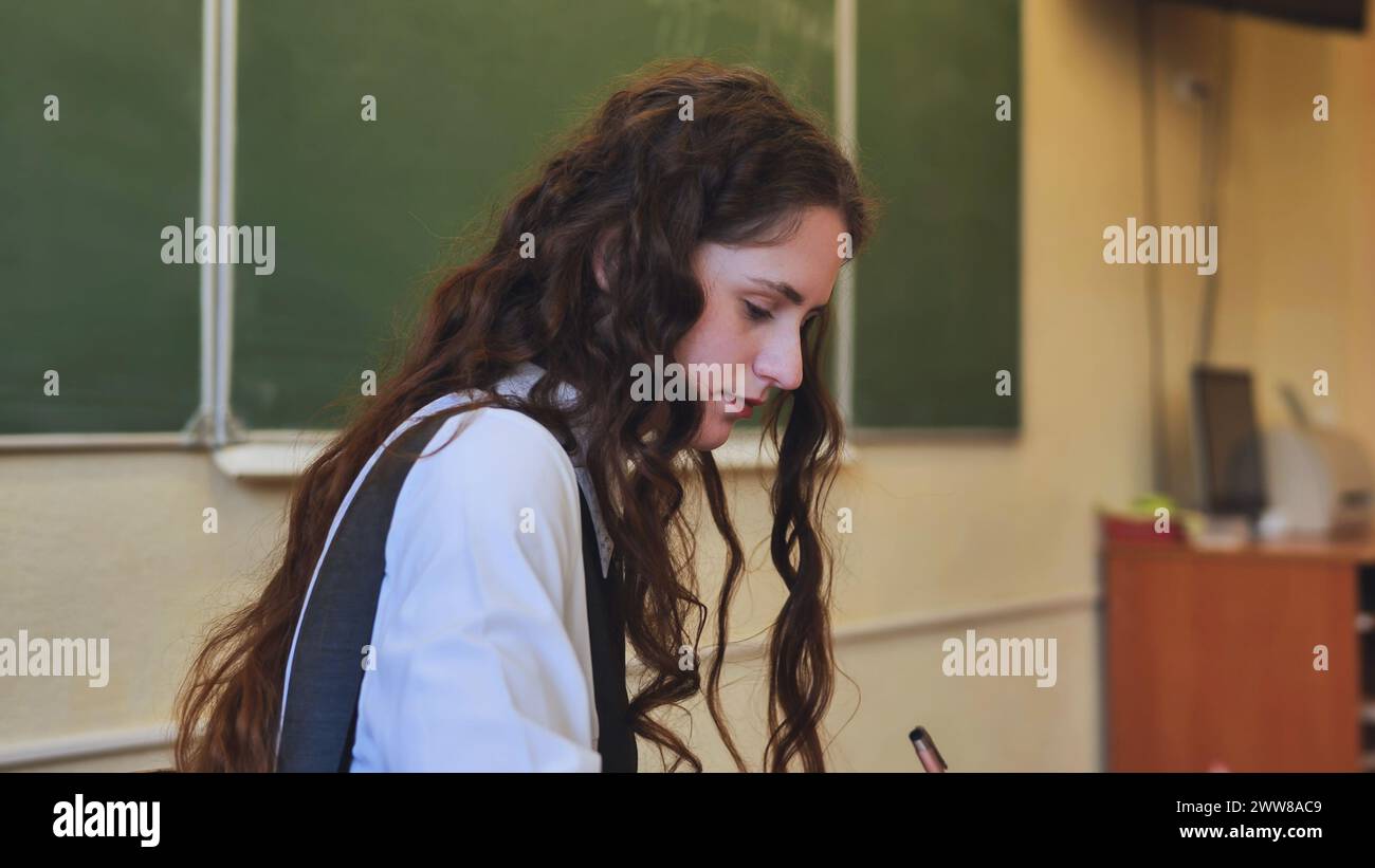 Schoolgirl as a teacher sits at a desk and writes something Stock Photo ...