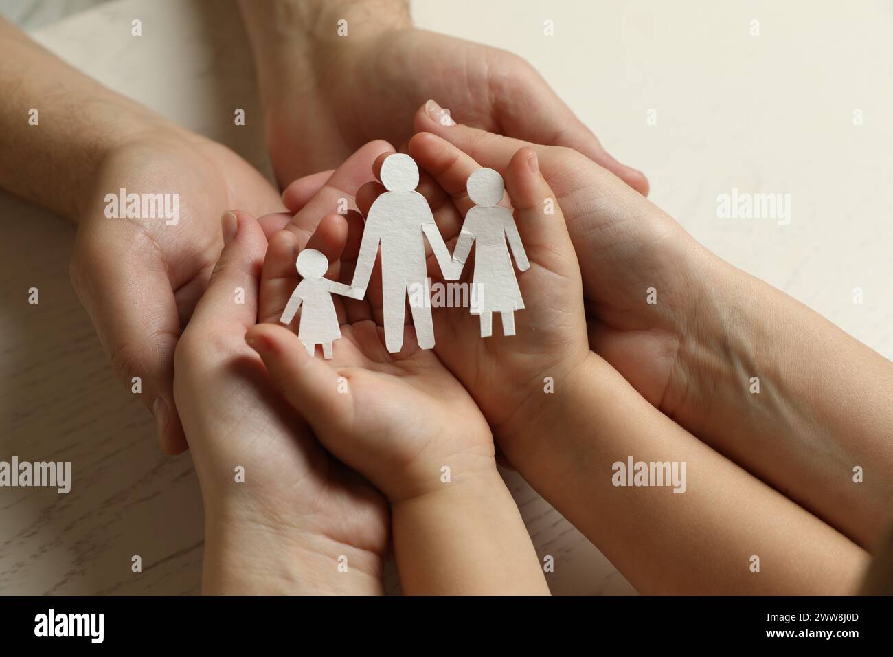 Parents and child holding paper cutout of family at white wooden table, closeup Stock Photo