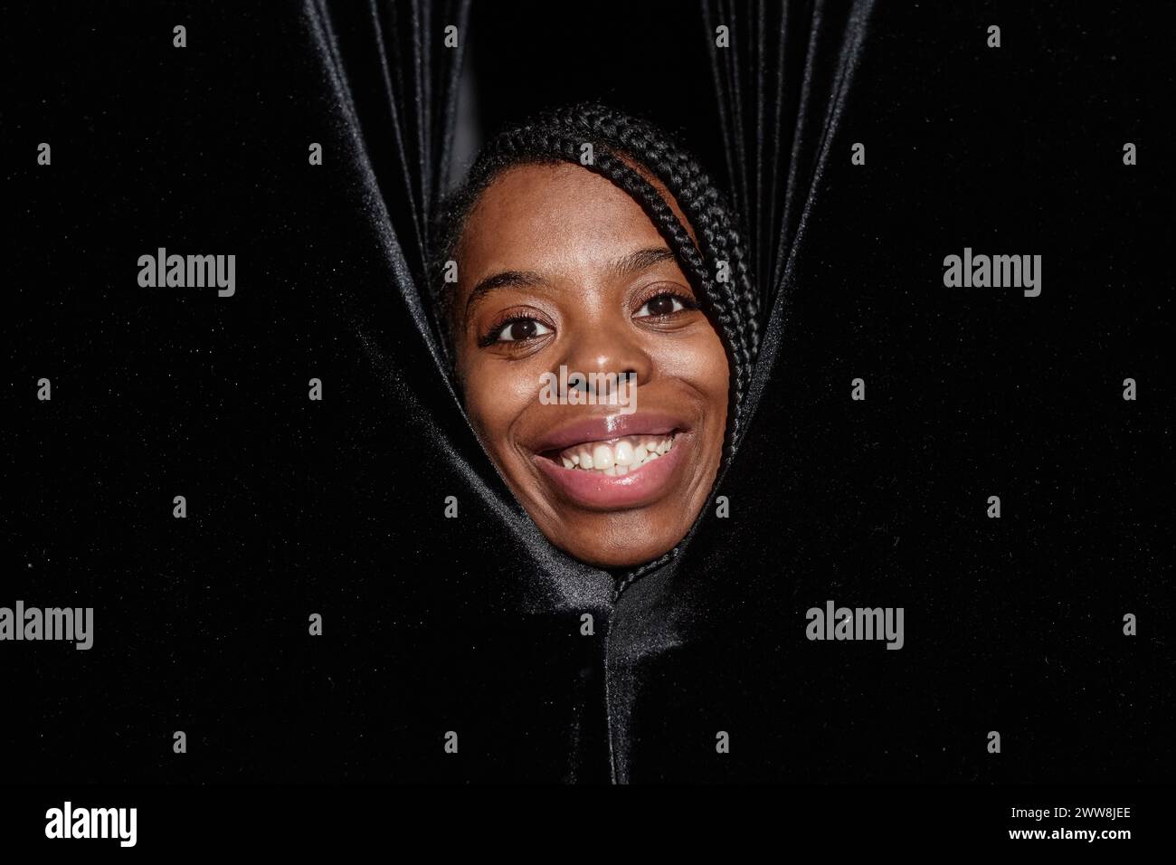 Close up of smiling African American woman peeking from curtains on theater stage and looking at camera Stock Photo