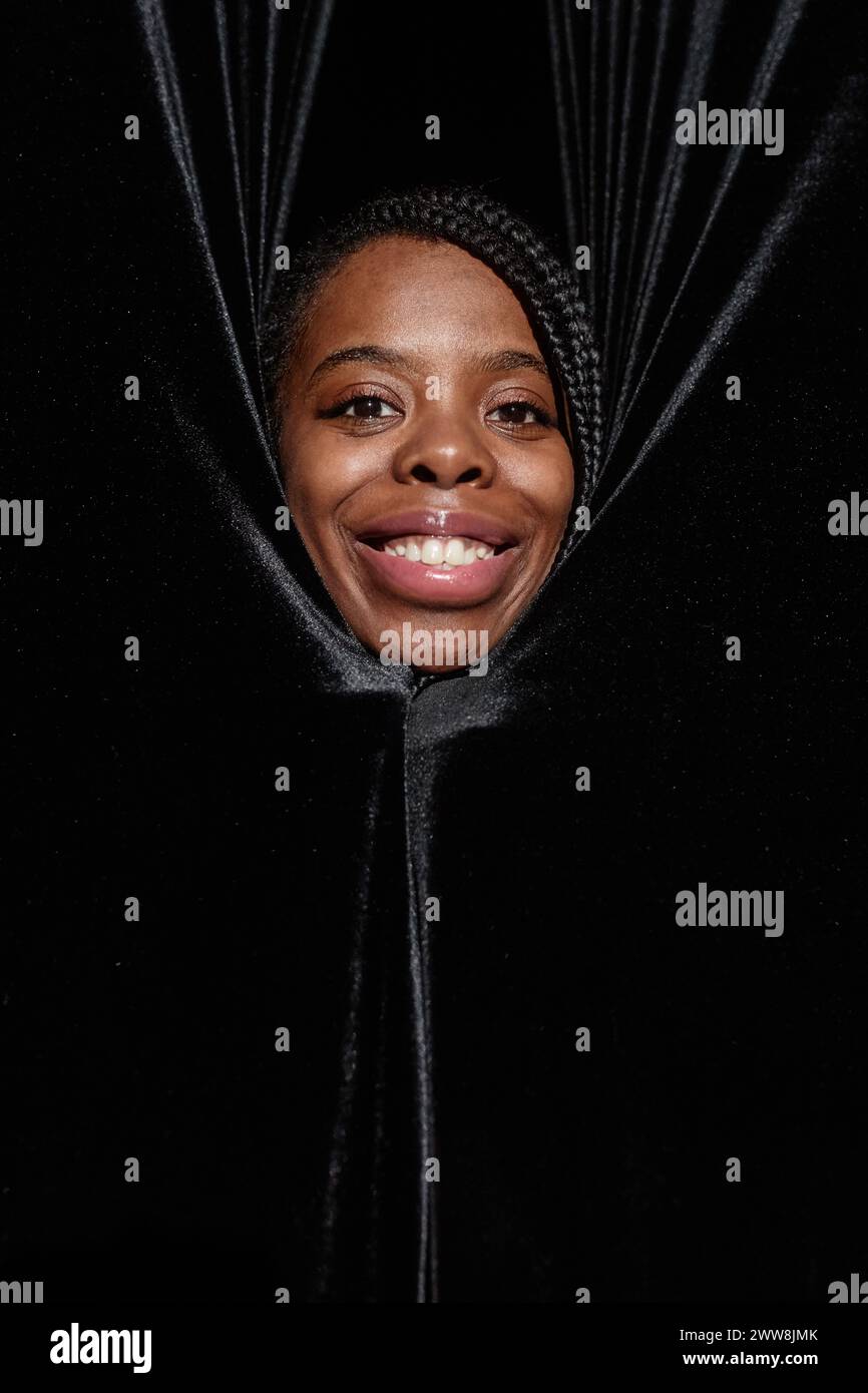 Vertical portrait of smiling Black woman peeking from curtains on theater stage Stock Photo