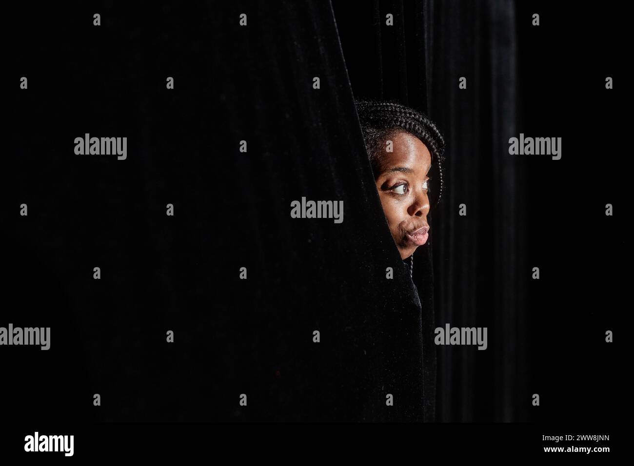 Young African American woman peeking from curtains looking at theater stage, copy space Stock Photo