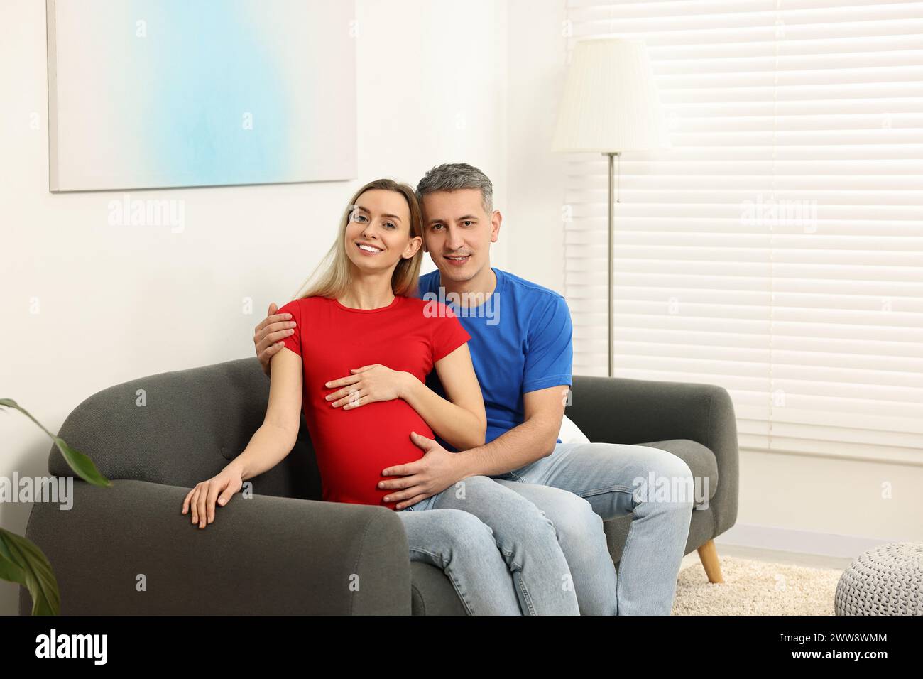 Young family housing concept. Pregnant woman with her husband on sofa at home Stock Photo