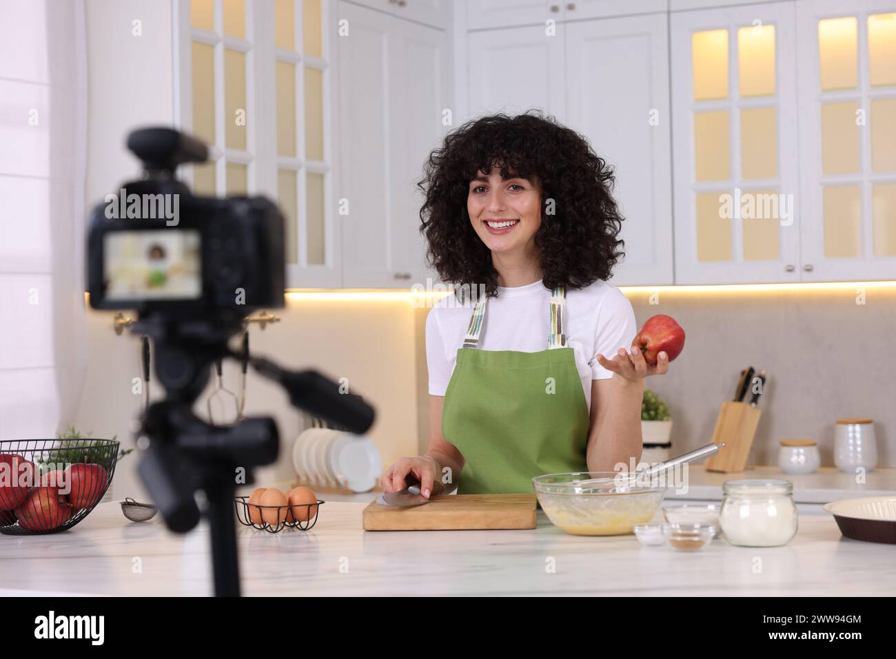 Smiling food blogger explaining something while recording video in kitchen Stock Photo