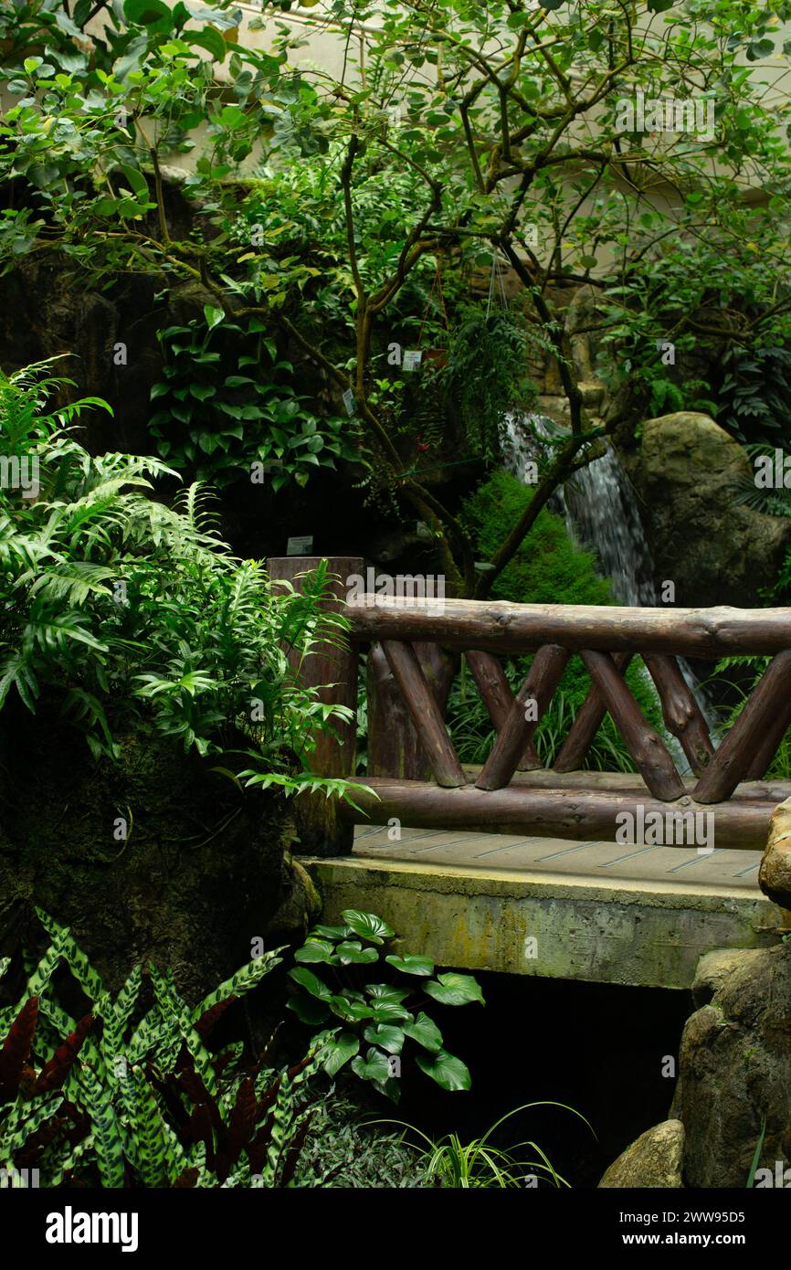 A bridge crosses an artificial stream flowing from a waterfall in the background. Stock Photo