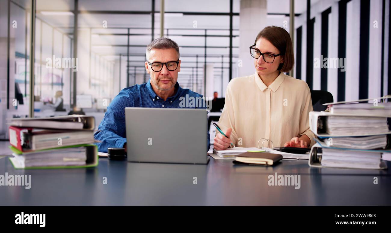 Two Businesspeople Calculating Invoice In Office While Using Laptop Stock Photo