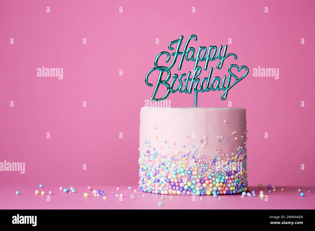 Celebration birthday cake with happy birthday cake pick against a pink background Stock Photo