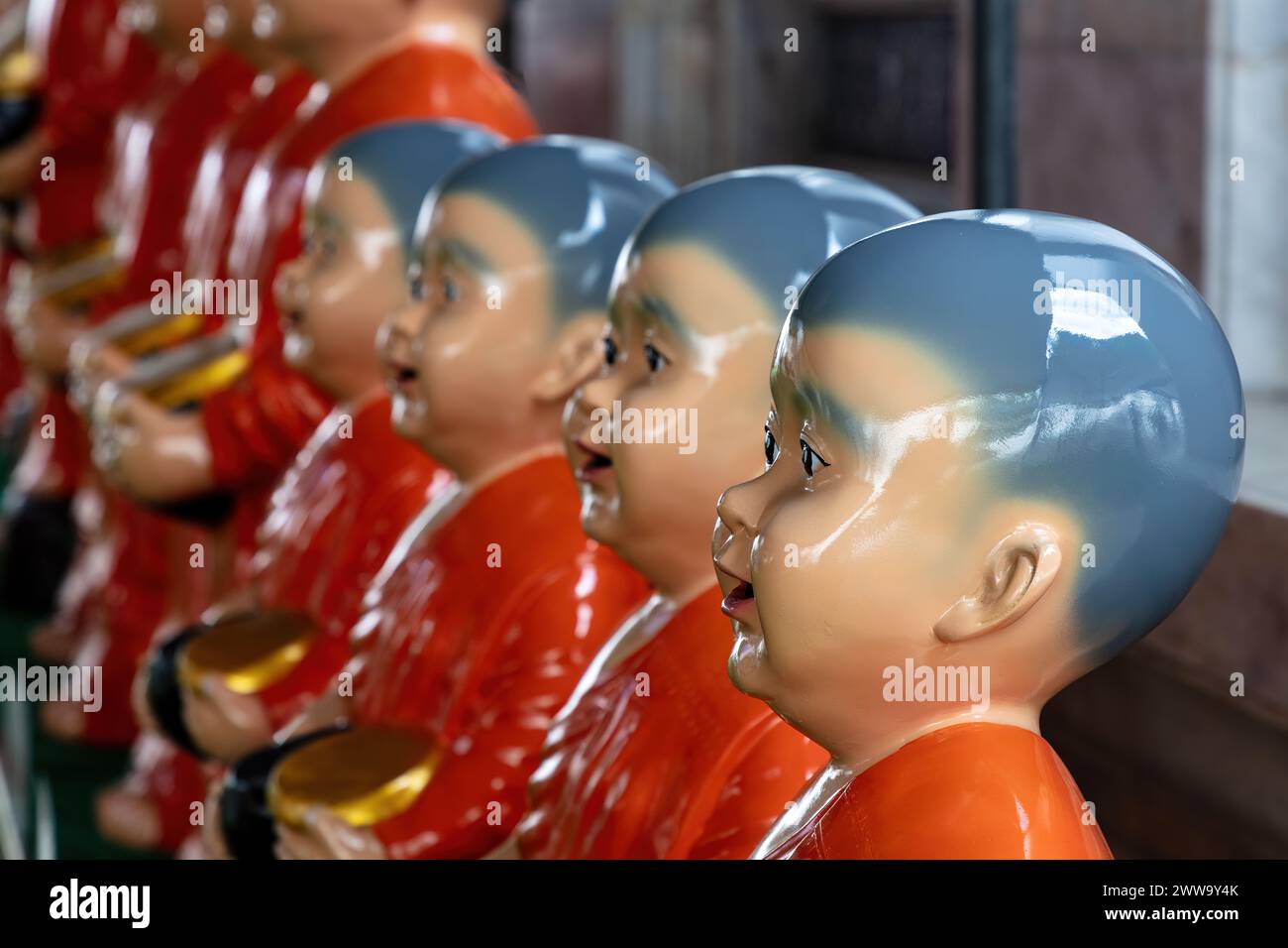 Line of statues depicting monks at Wat Rakhang (Temple of the Bells) in Bangkok, Thailand. Wearing red robes, holding golden bowls, shaved heads. Stock Photo