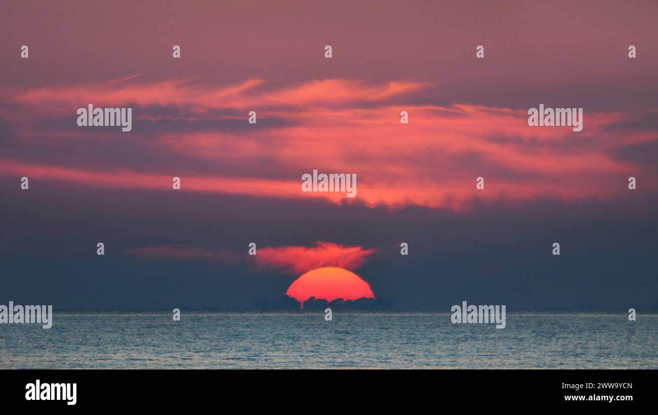 Close-up of a sunset in Florida, Pacific Ocean with a couple of light clouds in a pastel pink sky,sun disappearing behind the horizon ,copy space Stock Photo