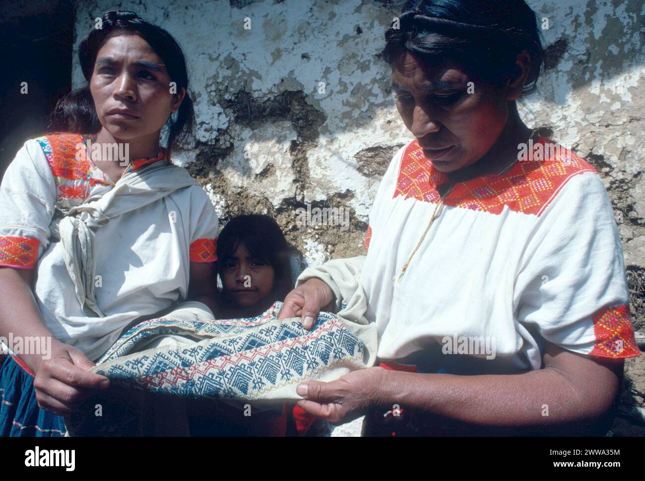 Chamula Tzotzil speaking Maya Indian woman weavers inspect the workmanship and brocaded design on a 100 year old huipil (Maya blouse) that was studied and found to encode an ancient Maya date. The ancient huipil was made on a traditional backstrap loom, just like the looms used by traditional Maya weavers today.  Huipils depicted on Late Classic (AD 600-900) clay figurines are little changed from those worn today.  Photographed on November 15, 1978 in San Juan Chamula, Highland Chiapas, southern Mexico. Stock Photo