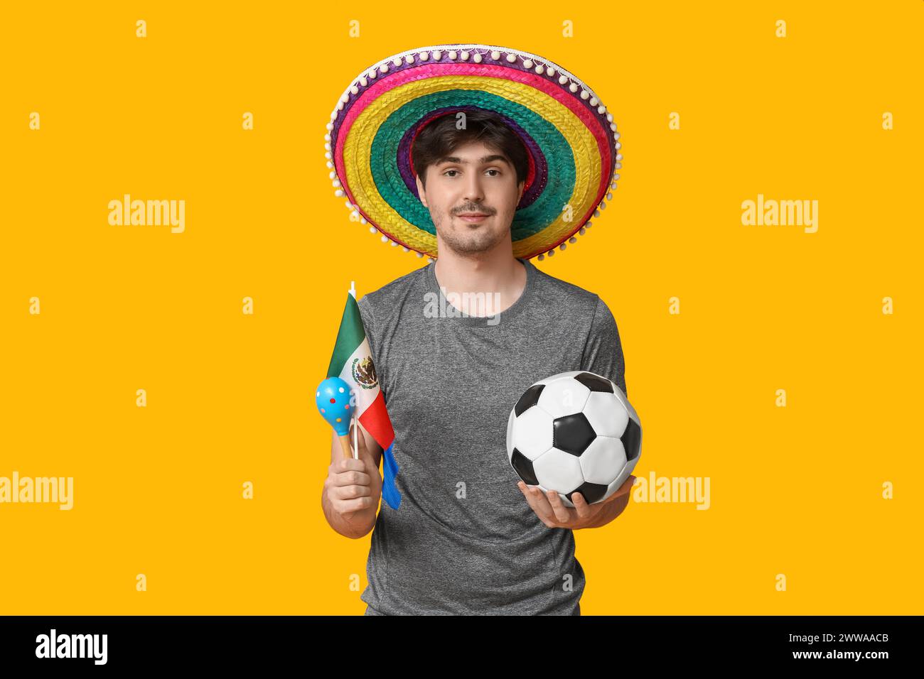 Young male football player with sombrero, soccer ball, flag of Mexico and maracas on yellow background Stock Photo