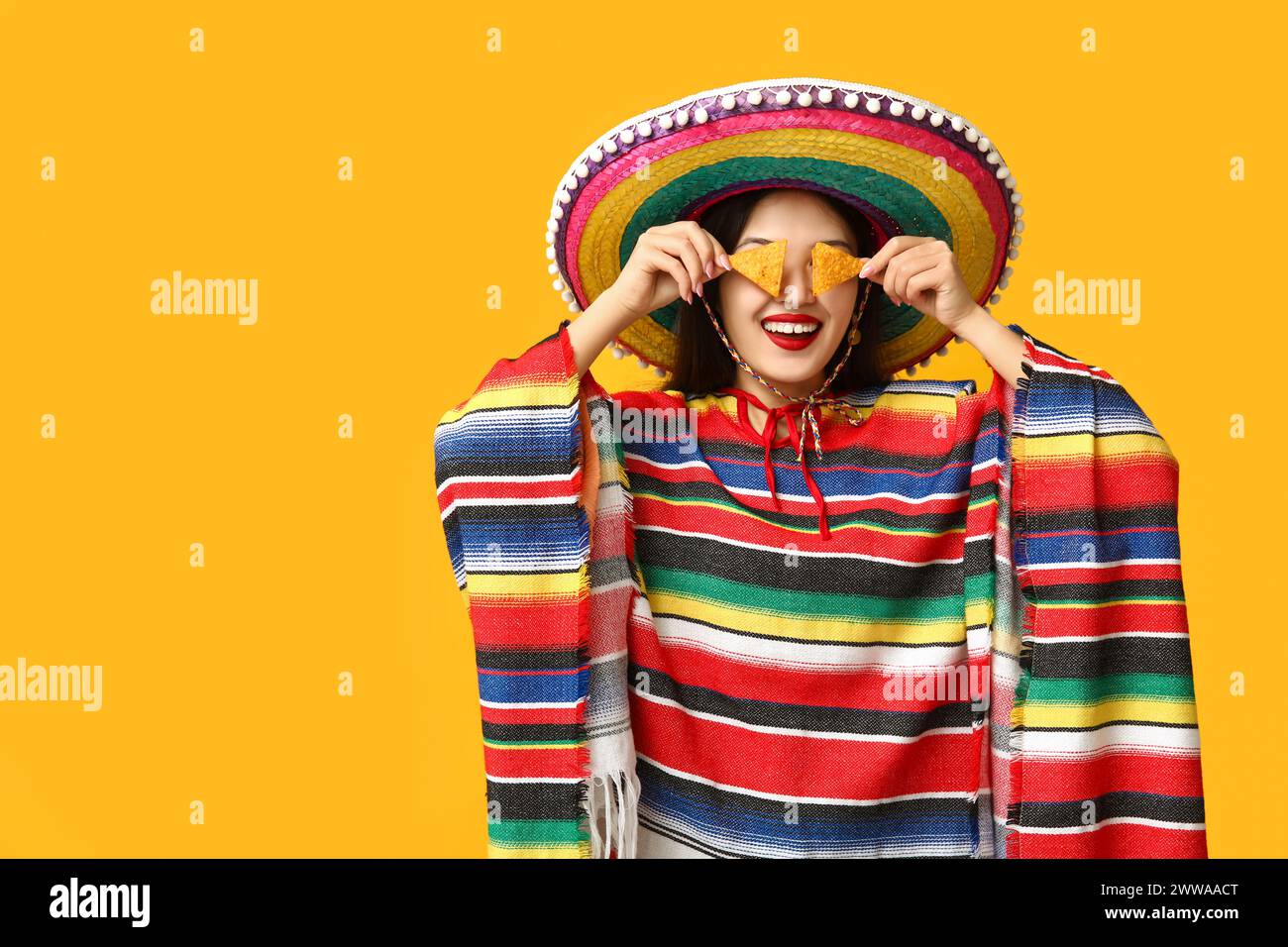 Portrait of young woman in colorful poncho and sombrero covering eyes