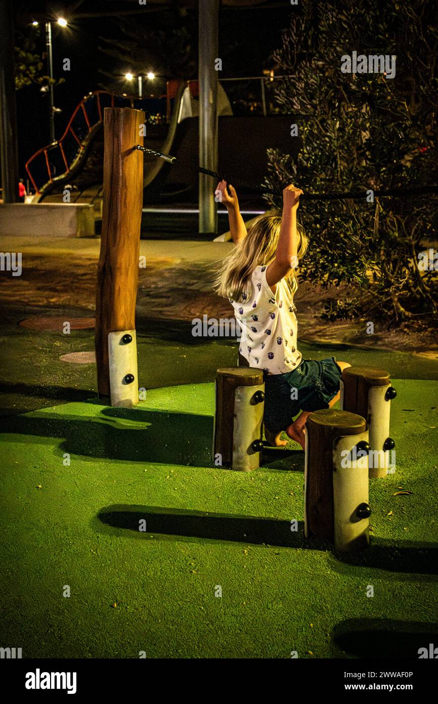 A child swinging with glee in a brightly lit nighttime playground. Stock Photo