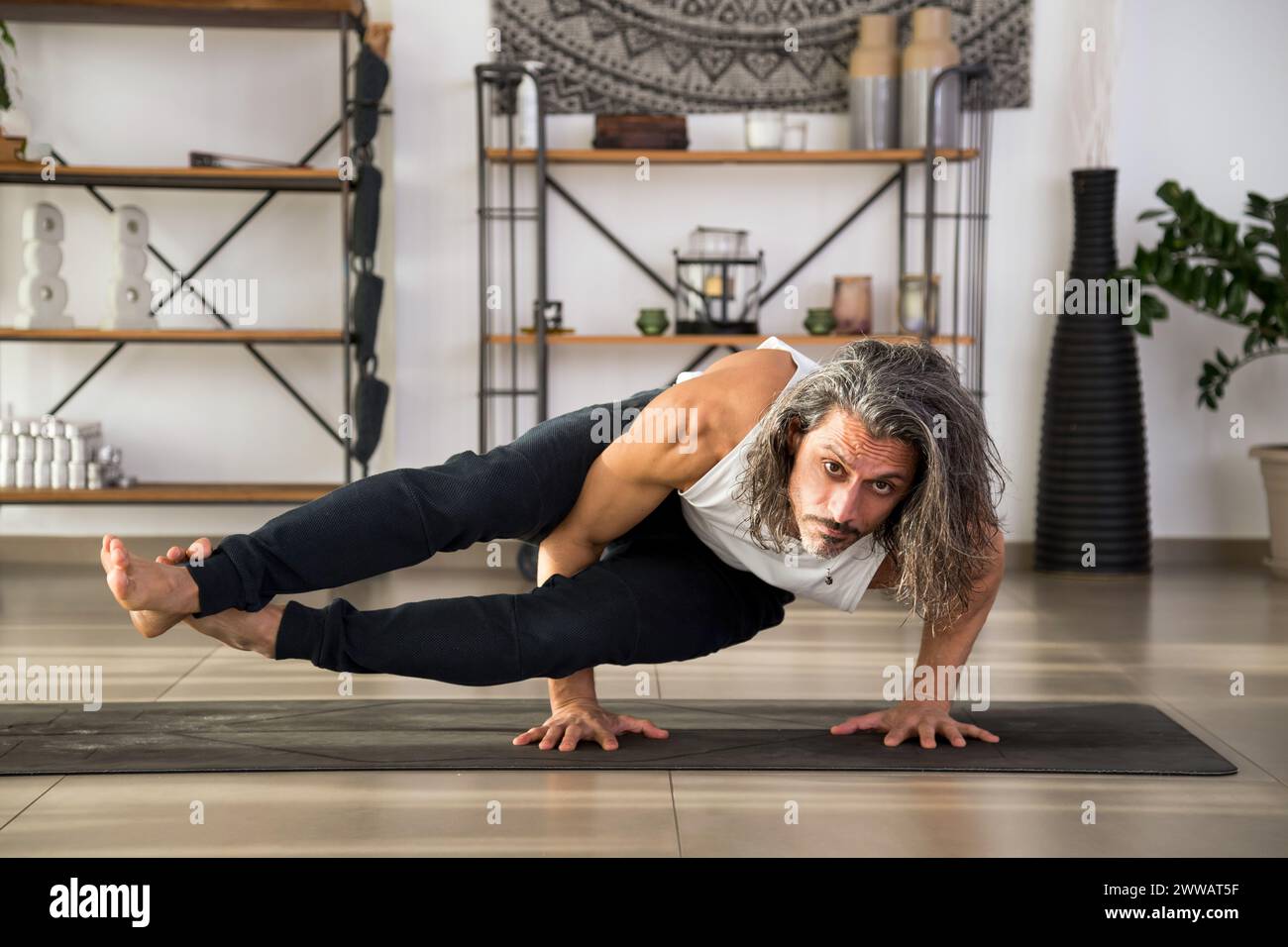 Focused adult male doing Eight Angle asana on mat while practicing fitness exercise at home Stock Photo