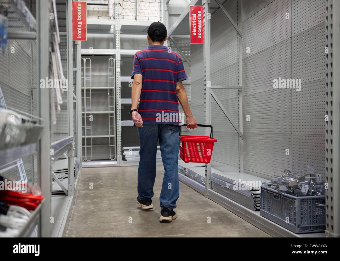 Man carrying a shopping basket, walking among the empty shelves. Stores closing down during the economic depression. Stock Photo