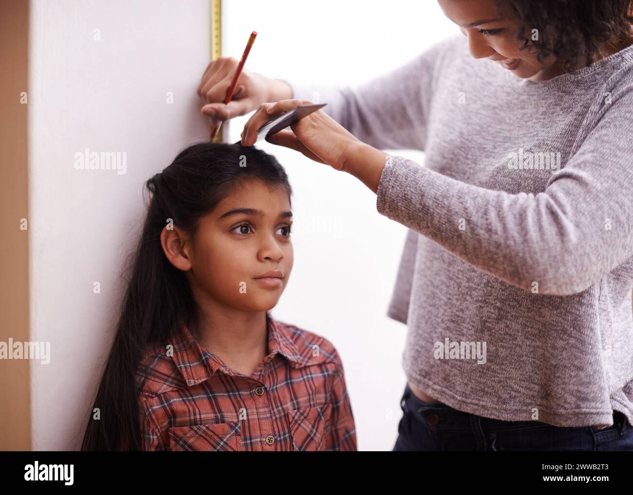 Mother, child and measuring height at wall for growth development in home for childhood, love or bonding. Female person, daughter and pencil with Stock Photo