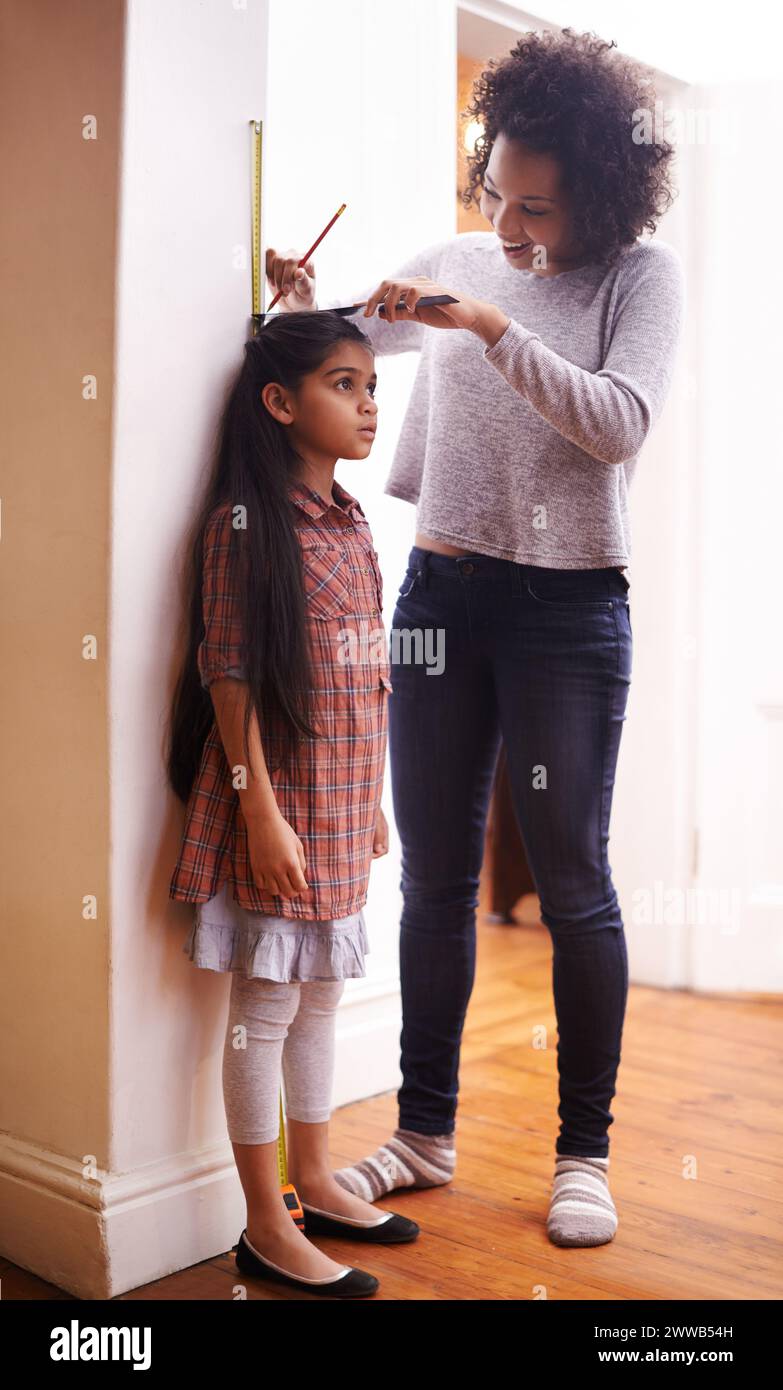 Parent, child and measuring height with ruler at wall for growth development in home for childhood, love or bonding. Female person, daughter and Stock Photo