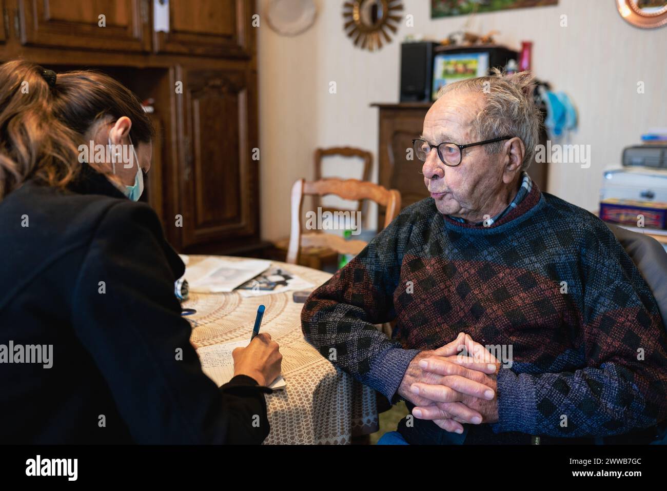 Home care by a nurse who fills out the coordination notebook for a 90-year-old senior and speaks with him. Stock Photo