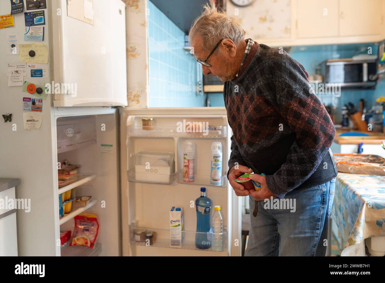 90-year-old senior in his kitchen looking for a dessert in his fridge. Stock Photo