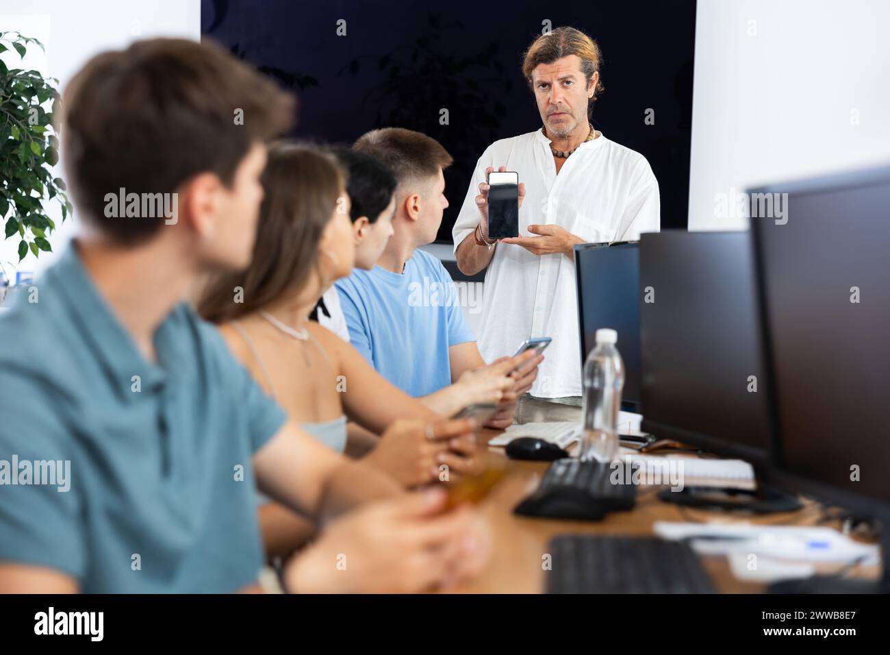 During computer courses, male teacher with mobile phone explains to ...