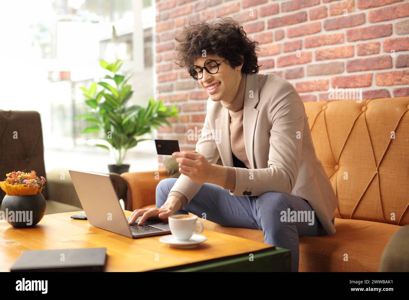 Man sitting in a cafe using a laptop computer and holding a credit card, online shopping concept Stock Photo