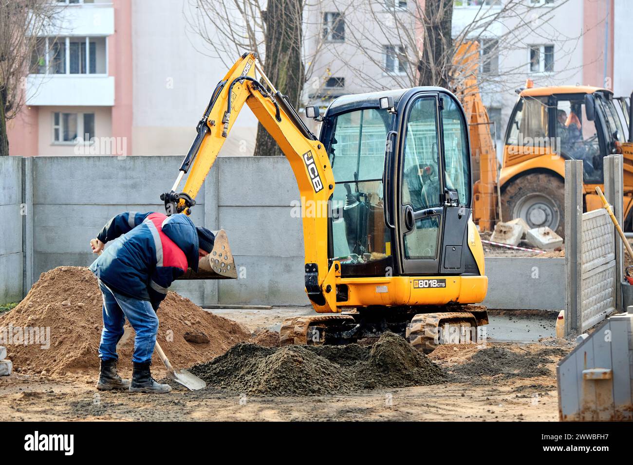 Grodno, Belarus - November, 22 2021: JCB 8018 CTS excavator digging sand and concrete at construction site with construction workers with shovels Stock Photo