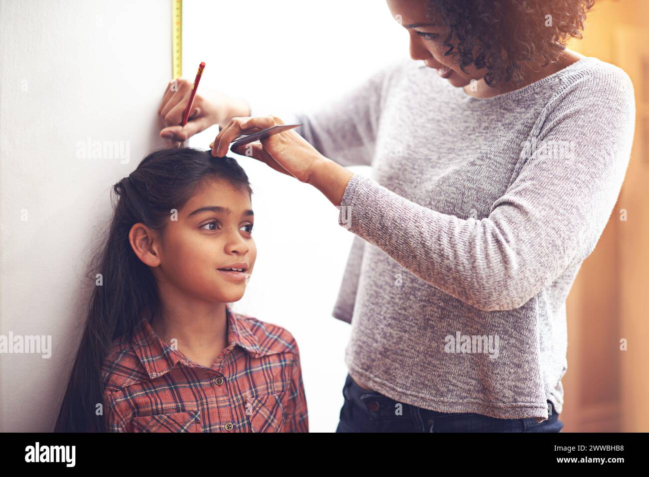 Mother, child and measuring height with ruler at wall for growth development in home for childhood, love or bonding. Female person, daughter and Stock Photo