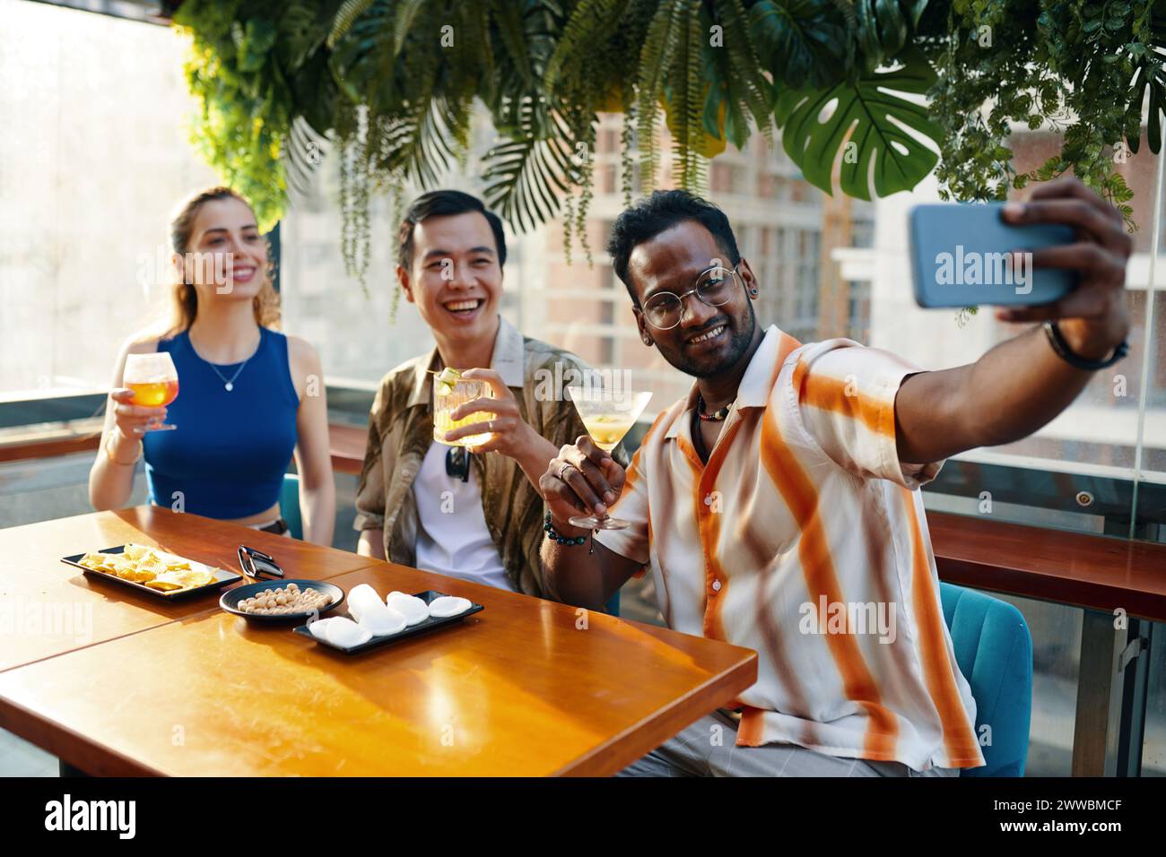 Excited man taking selfie with friends when sitting at table in bar Stock Photo